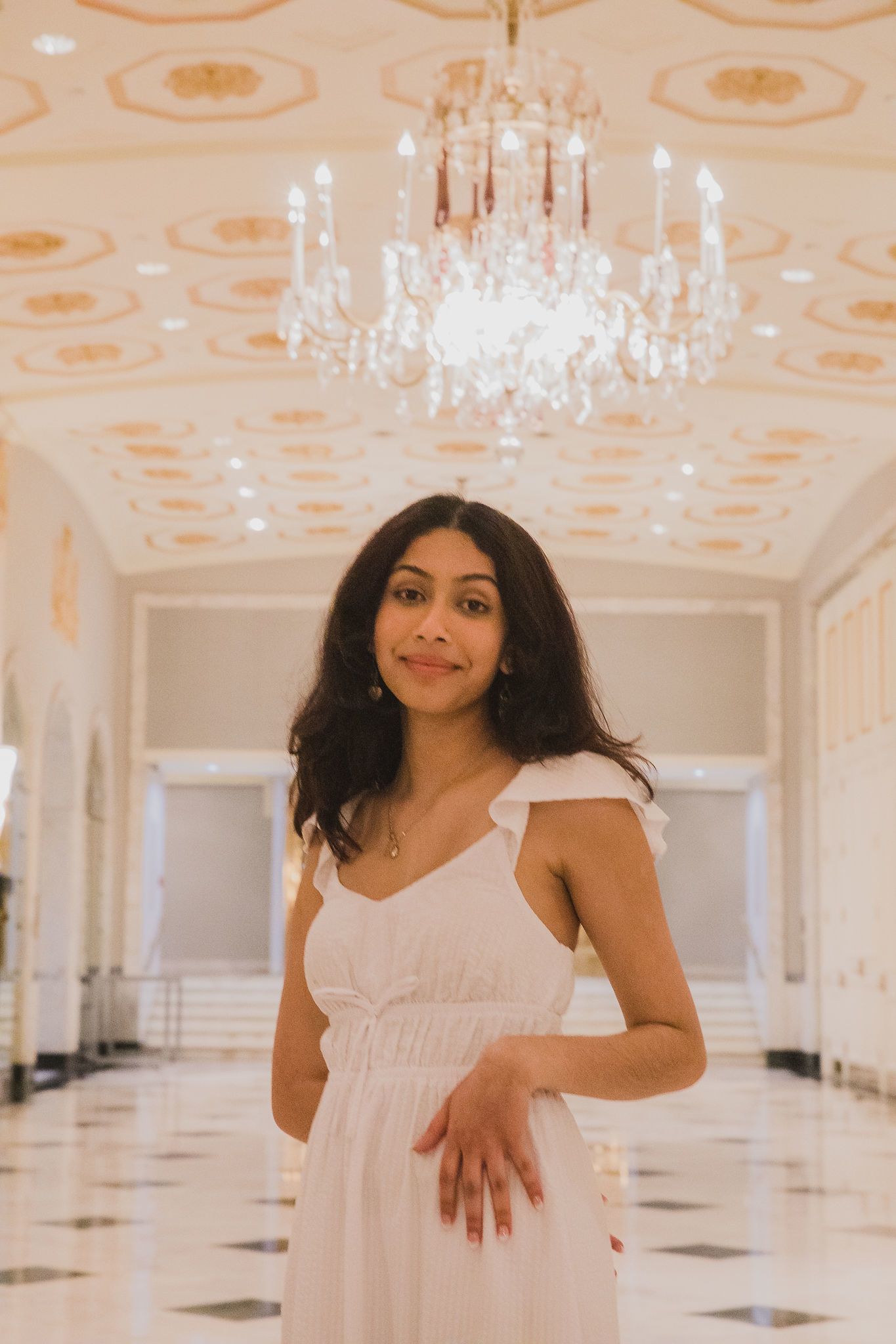 Anusha Nadkarni, an Indian woman in a white dress standing underneath a chandelier and smiling.